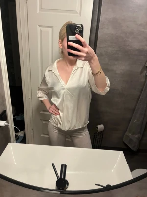 Vit satinblus med v-ringning - Säljer en stilren vit blus i satinliknande material med v-ringning och avslappnad passform. Blusen har långa ärmar och bred krage som ger en trendig look. Perfekt att matcha med både jeans och kjol för en chic outfit. Storlek L men passar mig som har xs-s i storlek.