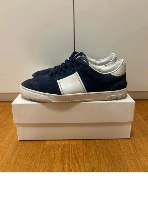 Valentino flycrew  - Snygga sneakers från Valentino i mörkblå mocka med vita detaljer och snörning. Klassisk låg modell med vit sula och blå logga på plösen. Perfekta för dig som vill ha en stilren och exklusiv look.