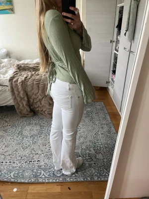 Ljusgrön omlottopp med knyt - Trendig ljusgrön omlottopp med djup v-ringning och långa ärmar. Toppen har knyt i ryggen och är tillverkad i ett lätt, krinklat material som ger en avslappnad känsla. 