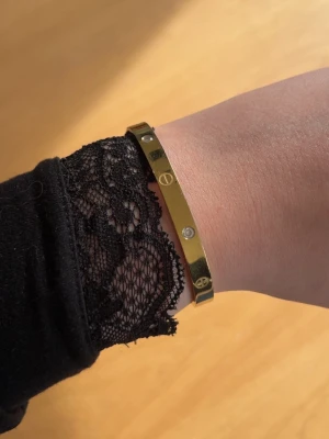 Guldigt armband med stenar - Snyggt och stilrent armband i guldfärgad metall med infällda klara stenar och ingraverade detaljer runt om. Armbandet har en klassisk, rund form och passar perfekt för dig som gillar minimalistisk men ändå lyxig stil. Köpt i Spanien!! 