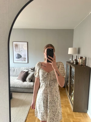 Blommig kortklänning med puffärm - Söt kortklänning från H&M med ljus botten och små blommor, puffärmar och snörning framtill. Linen blend. Använd endast ett par gånger