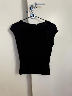 Svart tight topp med kort ärm - En enkel och stilren svart topp med tight passform och korta ärmar. Toppen har rundad halsringning och är perfekt att matcha med jeans eller kjol. Materialet känns mjukt och stretchigt.