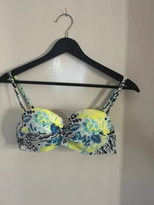 Blommig bikiniöverdel i blå och gul - Snygg bikiniöverdel med blommigt mönster i blått, gult och vitt. Har justerbara axelband och bygel för extra stöd. Perfekt för stranddagar och sommarhäng. Materialet känns mjukt och följsamt mot huden. Super snygg och skön. Perfekt! Sista bilden visar ett litet märke men det kommer/borde försvinna i nästa tvätt eftersom den legat i låda och fått det ungefär så. Har bundle rabatt! 