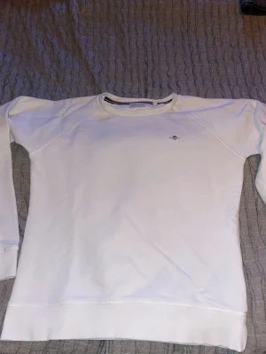 Vit sweatshirt från Gant - Klassisk vit sweatshirt från Gant med rund halsringning och diskret logga broderad på bröstet. Tröjan har långa ärmar, ribbade muddar och är tillverkad i mjukt bomullsmaterial. Perfekt för en clean och stilren look.