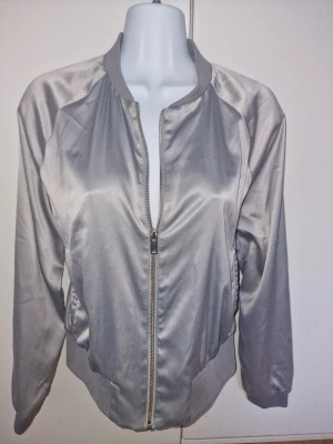 Silvrig bomberjacka från Gina Tricot - Snygg silvrig bomberjacka från Gina Tricot med glansigt tyg. För dig som vill ha en stilren och trendig look.