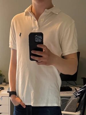 Ralph Lauren pike.  - Säljer en vit piké från Ralph Lauren. Den har små hål vid ärmarna och lite slitet där nere men absolut inget som märks vid användning. Den har en liten fläck nere på baksidan vilket heller inte märks vid användning. Storlek Small/S classic fit.