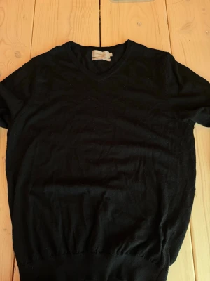 Svart stickad tröja med Merino Ull - En klassisk svart stickad tröja med V-ringad hals och långa ärmar. Tröjan har ribbade muddar vid ärmslut och nederkant. Perfekt basplagg i garderoben och enkel att matcha med olika stilar. Äkta merino ull i storlek L