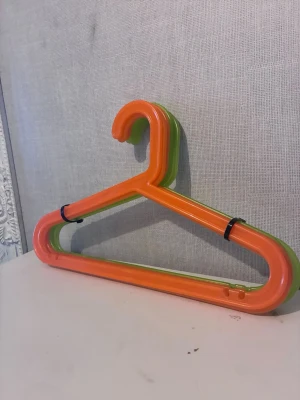 Färgglada galgar i plast - Säljer ett set med plastgalgar i neonorange och neongrönt. Galgarna har en klassisk trekantig form och är perfekta för att hänga upp kläder i garderoben. 2st gröna och 2st orange
