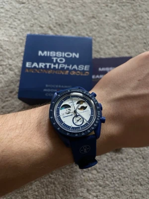 Omega x Swatch Moonshine Gold Snoopy - Snygg blå klocka från Omega x Swatch Mission to Earthphase Moonshine Gold. Klockan har blå boett och armband, vit urtavla med detaljer i blått och guld samt flera subdials. Tillverkad i biokeramik och levereras i originalförpackning.