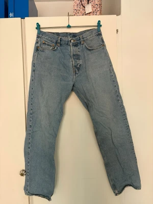 Ljusblå raka jeans från Weekday - Klassiska ljusblå jeans från Weekday med rak passform och hög midja. Jeansen har fem fickor, gylf med dragkedja och knapp samt tydliga sömmar. Tillverkade i slitstark denim av bomull. Perfekta för en avslappnad och tidlös stil.