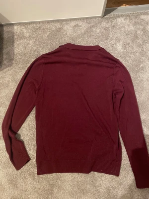 Vinröd stickad tröja från Studio - Mysig vinröd stickad tröja från Studio med lång ärm och ribbade muddar. Tröjan har en enkel, klassisk design och är perfekt för lager på lager. Tillverkad i mjukt material som känns skönt mot huden.