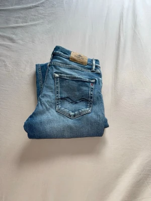Replay - Säljer ett par klassiska blå jeans från Replay med snygg tvätt och raka ben. Jeansen har snygga slitningar som ger en vintage trendig look.
