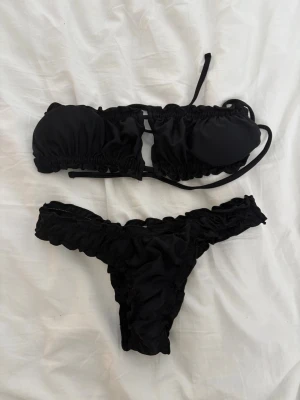 Svart bandeau bikini med volang - Säljer en svart bandeau bikini från Shein med volangdetaljer och scrunchad design🌸 stl M i både överdel och underdel🌸Överdelen har knyt i ryggen🌸Aldrig använd, endast testad🌸