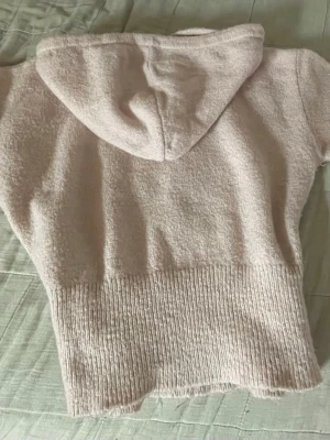 Ljusrosa stickad hoodie - Mysig ljusrosa hoodie i stickat material med korta ärmar och bred ribbad kant nedtill. Huvan har dragsko och tröjan har en avslappnad passform. Perfekt för en chill och trendig look.