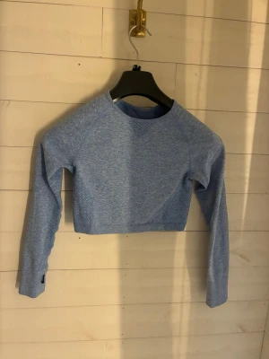 Blå cropped träningströja relode - Cropped långärmad träningströja i ljusblått från relode. Tröjan har rund halsringning, meshdetaljer för extra ventilation och tumhål vid ärmsluten. Perfekt för gymmet eller löprundan, tillverkad i stretchigt funktionsmaterial.