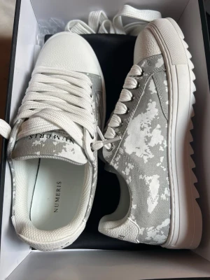 Gråvita sneakers från Numeris - Snygga sneakers från Numeris i grått och vitt med camomönster. Skorna har vita snören, grov sula och detaljer i textil och syntet. Perfekta för dig som gillar streetstyle och vill sticka ut med ett unikt mönster.