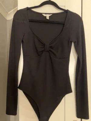 HM body - Säljer denna svarta bodyn från hm med en ”rosett” vid urringningen, nyskick💕 (Ej tvättad på bilden men tvättad innan köp)