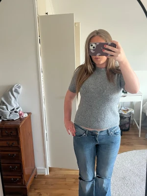 Grå stickad t-shirt i ullblandning - En enkel och stilren grå stickad t-shirt med korta ärmar och rund hals. Tröjan har ribbade muddar vid ärmslut och nederkant. Perfekt för lager på lager och passar till det mesta. Materialet känns mjukt och har en lätt melerad look.