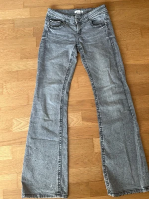 Grå bootcut jeans med fickor - Snygga grå bootcut jeans med klassiska fem fickor och knappgylf. Jeansen har en lätt tvättad look och raka ben som går ut något nedtill. Passar perfekt till en avslappnad stil och är tillverkade i mjukt denimtyg.