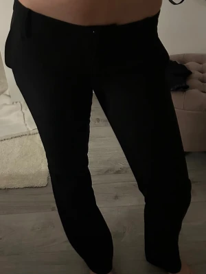 Svarta raka kostymbyxor - Säljer ett par svarta kostymbyxor med rak passform och klassisk midja. Byxorna har hällor för skärp och stängs med knapp och dragkedja. Perfekta för en clean och stilren look.