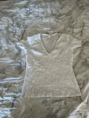 Vit ribbad v-ringad topp - Säljer en vit ribbad topp med v-ringning och korta ärmar. Tyget har en stretchig struktur och toppen sitter figurnära. Perfekt att matcha med jeans eller kjol för en enkel och snygg look.