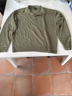 Olivgrön stickad tröja med krage - Säljer en olivgrön stickad tröja med klassisk krage och knappar vid halsen. Tröjan har långa ärmar, ribbstickade muddar och nederkant. Perfekt för dig som gillar en avslappnad men ändå stilren look.