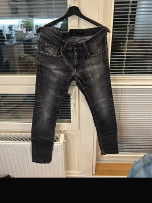 Tiger of Sweden Jeans - Säljer ett par svarta  jeans med snygga slitningar och tvättade detaljer. Jeansen har klassiska fem fickor, dragkedja och knapp framtill samt bakfickor med markerade sömmar. Perfekt för dig som gillar en modern och cool look.