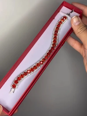 Armband med röda glittriga pärlor - Snyggt armband med stora röda glittriga pärlor infattade i silverfärgad metall. Armbandet har en klassisk tennisdesign och gnistrar rejält tack vare de många stenarna. 