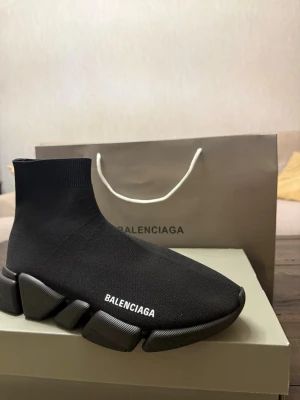 Svarta Balenciaga sneakers - Stilrena svarta sneakers från Balenciaga med tydlig logga på sidan. Skorna har chunky sula och är tillverkade i en mix av textil och syntetmaterial. Levereras i originalkartong med dustbag och certifikat. Perfekta för dig som gillar exklusiv streetwear.