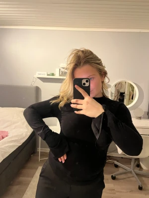 Svart polotopp med långa ärmar - Snygg svart polotopp med långa ärmar och figurnära passform. Toppen har en medelhög krage och är tillverkad i ett mjukt material som känns bekvämt mot huden. Slits i ärmarna och insydd i midjan