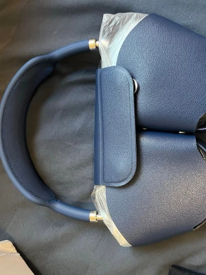 Blå over-ear hörlurar med fodral - Snygga over-ear hörlurar i matt mörkblå färg med matchande skyddsfodral. Hörlurarna har vadderad bygel och öronkåpor i konstläder för extra komfort. Medföljer USB- och AUX-kabel för laddning och anslutning. Perfekt för musik, gaming eller film.