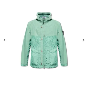 Mintgrön vindjacka från Stone Island - Snygg mintgrön vindjacka från Stone Island med hög krage och dragkedja framtill. Jackan har knappslå, två sidofickor och den klassiska logotypen på ärmen. Tillverkad i lätt, glansigt material som ger en sportig look.