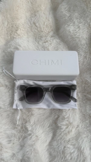 Grå transparenta solglasögon från CHIMI - Snygga solglasögon från CHIMI med transparent grå båge. Kommer med originalfodral och tygpåse. Säljer då de inte används! Glasögonen är i super bra skick, fodralet har någon fläck på sig som synd på tredje bilden men går fortfarande väldigt bra att använda! 