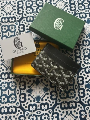 Svart kortfodral  - Stilrent svart kortfodral från Gayard med ikoniskt mönster i vitt och grått. Fodralet har flera fack för kort och är tillverkat i läder och canvas. Perfekt för dig som vill ha något exklusivt och snyggt i fickan. Levereras med originalask och certifikat.