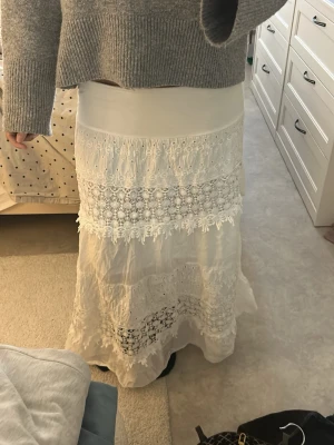 Vit långkjol med spetsdetaljer - Romantisk vit långkjol med flera lager av spets och broderade detaljer. Kjolen har en bred midjeresår och vackra volanger som ger en bohemisk känsla. Perfekt för dig som gillar en feminin och avslappnad stil. Står ingen storlek men passar mig som brukar ha xs/s, vet tyvärr inte heller vart den är ifrån då den är köpt i en second hand butik. Skriv om de finns några frågor☺️💗💗