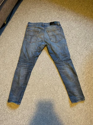 Blå slim fit jeans från tiger of sweden - Säljer ett par blå slim fit jeans från tiger of sweden med klassisk femficksdesign och snygga slitningar. Jeansen har en modern passform och är tillverkade i denim med stretch för extra komfort. Perfekt för dig som gillar en stilren look. Strl w31 L30