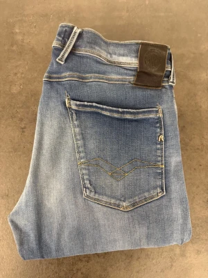 Ljusblå raka jeans med kontrastsömmar 34/34 - Snygga ljusblå jeans med raka ben och slitningar på framsidan. Jeansen har klassiska fem fickor, kontrastsömmar och en läderpatch bak i midjan. Materialet är mjukt denim och passformen är relaxed. Perfekta för en avslappnad stil.