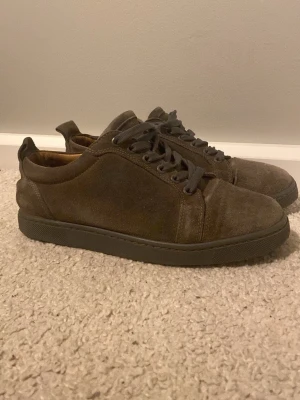 Christian louboutin  - Stilrena sneakers i brun mocka med matchande bruna skosnören och en unik röd sula. Lågt skaft och klassisk design som passar till det mesta. Skorna har en enkel och clean look med diskreta sömmar och rundad tå.