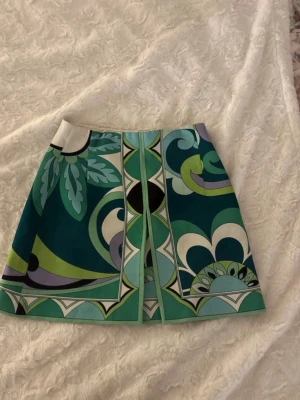 Mönstrad kortkjol från Zara - Säljer en färgstark kortkjol från Zara med coolt grafiskt mönster i grönt, blått, vitt och svart. Kjolen har en A-linjeform och är tillverkad i ett mjukt bomullsmaterial. Perfekt för dig som vill sticka ut med en unik look! Kjolen har dessutom aldrig använts 