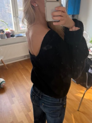 Svart stickad tröja med v-ringning baktill - Snygg svart stickad tröja med djup v-ringning i ryggen. Tröjan har en lös passform och långa ärmar, perfekt att styla med jeans. Mjuk och skön, passar dig som gillar en avslappnad men trendig look. Knappt använd. 