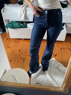 Mörkblå bootcut jeans high waist - Säljer ett par mörkblå bootcut jeans med hög midja och klassisk femficksmodell. Jeansen har en snygg, figurnära passform upptill och lätt utsvängda ben. Perfekta till sneakers eller boots och passar till många olika stilar.