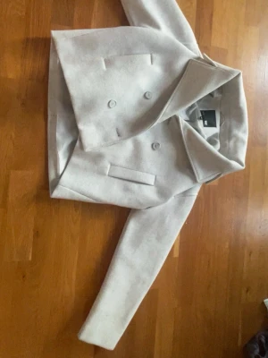 Ljusgrå dubbelknäppt rock 157 XS - Snygg ljusgrå kappa från 157 i storlek XS. Kappan har dubbelknäppning framtill, bred krage och raka fickor. Tillverkad i ett mjukt material med slät insida.