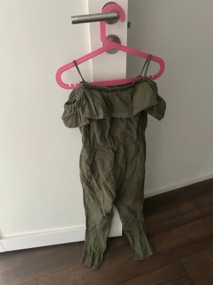 Olivgrön off shoulder jumpsuit - Trendig olivgrön jumpsuit med smala axelband och volang upptill. Off shoulder-modell i ett mjukt, skrynkligt tyg som ger en avslappnad look. Perfekt för dig som vill ha en enkel men snygg outfit. Inget synligt märke.
