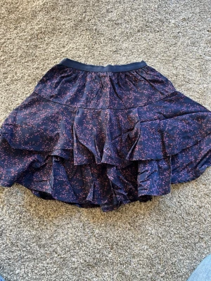 Mörkblå volangkjol med småmönster - Snygg mörkblå kortkjol med volanger och små rosa detaljer. 