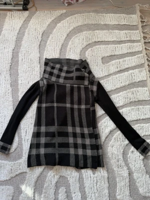 Svart och grå lång kofta med rutmönster - Snygg svart kofta med grått rutmönster och öppen front. Långa ärmar med mönstrade muddar och bred krage. Stickat och tjockt material. Knappt använd. Bodyflirt Boutique är märket. 