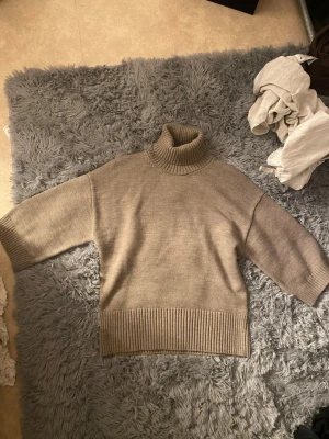 Beige stickad polotröja - Säljer en beige stickad polotröja med breda, trekvartsärmar och ribbade detaljer vid hals, ärmslut och nederkant. Tröjan har en avslappnad passform och är perfekt för lager-på-lager-stil. Materialet känns mjukt och mysigt.