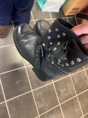 Svarta boots med nitar och spänne - Coola svarta boots i läder med rund tå, dekorerade med silvriga nitar och ett spänne vid ankeln. Perfekta för dig som vill ha en edgy stil och gillar detaljer som sticker ut.
