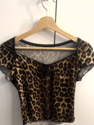 Leopardmönstrad mesh topp - Snygg croppad topp med leopardmönster och korta ärmar. Toppen har en liten rosett framtill och dekorativ kant vid halsen. Perfekt för dig som vill sticka ut med ett djuriskt print.