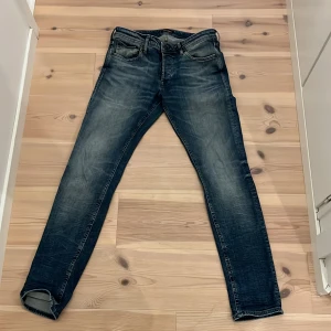 Mörkblå jeans från Jack & Jones - Säljer ett par mörkblå jeans från Jack & Jones med snygga detaljer och klassisk femficksdesign. Jeansen har normal passform och raka ben, tillverkade i bomull med en skön jeanskänsla. Perfekta för dig som gillar en tidlös look.