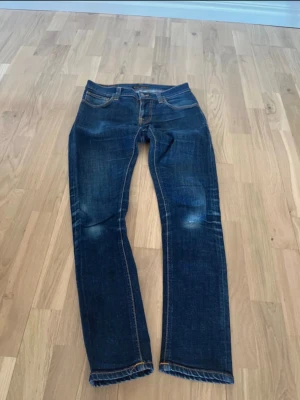 Nudie Jeans - Säljer ett par mörkblå jeans från Nudie Jeans med slitningar